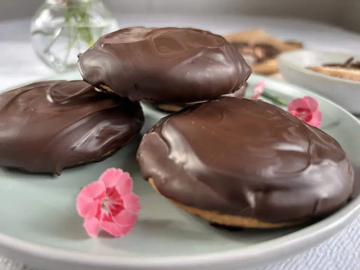 Tre choklad&ouml;verdragna biskvier p&aring; en ljusgr&ouml;n tallrik, med sm&aring; rosa blommor. Ett perfekt biskvier recept f&ouml;r fikat.