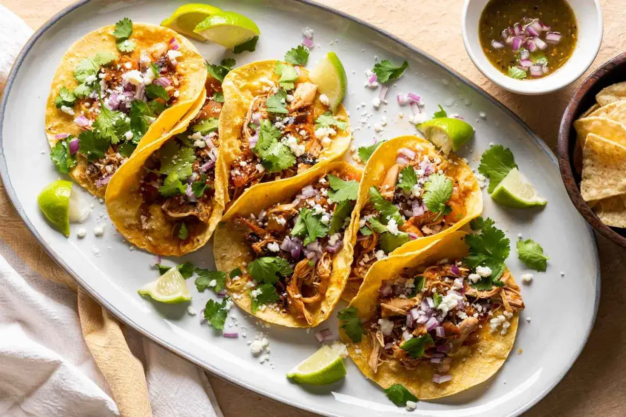 En tallrik med fem kycklingtacos, toppade med koriander, l&ouml;k och ost. Serveras med limeklyftor och en sk&aring;l salsa. Perfekt f&ouml;r ett snabbt tacos recept.