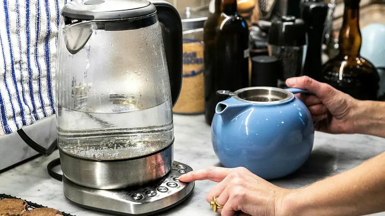 En person trycker p&aring; knappen f&ouml;r att v&auml;rma vatten i en vattenkokare, redo att dricka varmt vatten p&aring; morgonen. En bl&aring; tekanna st&aring;r bredvid.