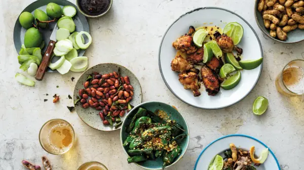 En härlig dukning med olika rätter av thai mat: kycklingvingar, friterade gröna paprikor, jordnötter och omogna mangos.