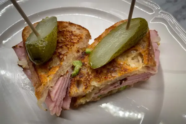En saftig reuben sandwich med skinka, surkål och rostat bröd, toppad med dillgurka.