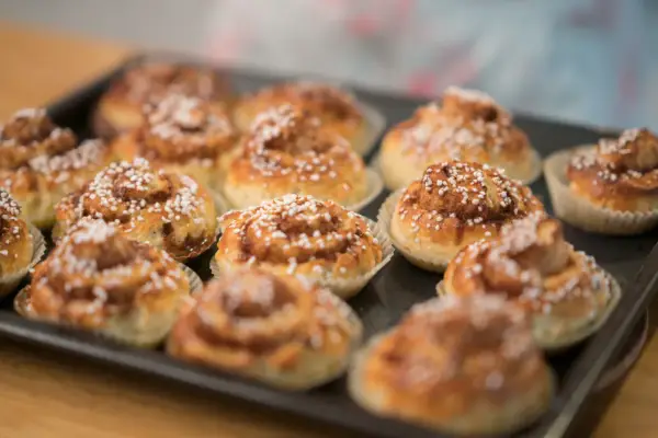 En plåt med nybakade glutenfria kanelbullar, toppade med pärlsocker. Doften av kanel sprider sig i köket.