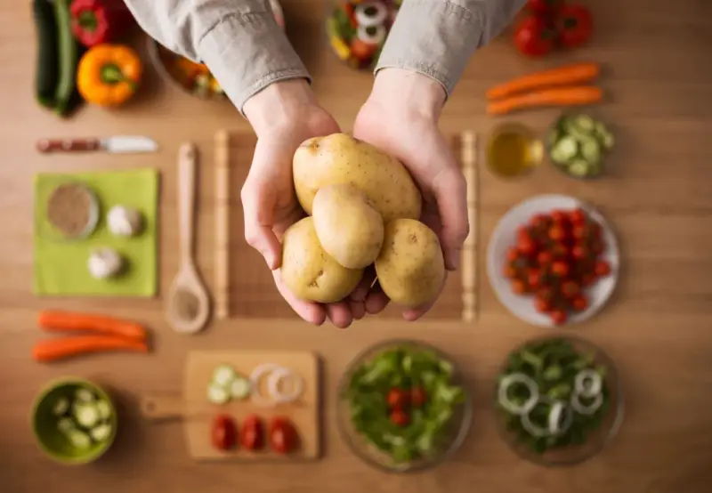 Händer håller färsk potatis, en del av en hälsosam måltid med grönsaker. Potatis nyttigt!