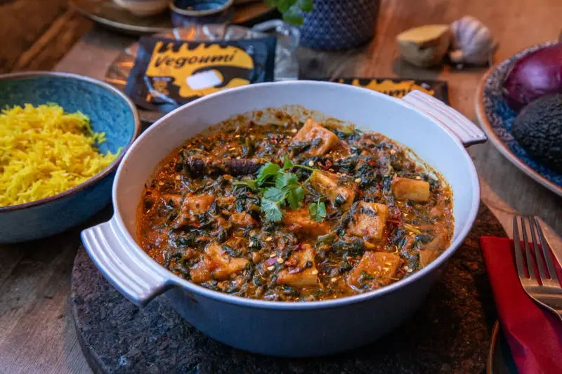 En krämig palak paneer med gyllene ris. Vegoumi-förpackning syns i bakgrunden.