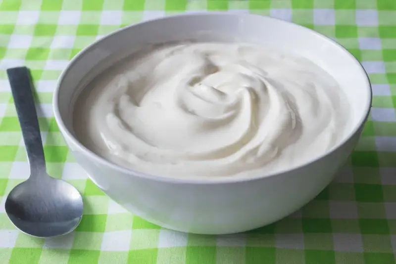 En skål med krämig yoghurt, redo att avnjutas. En sked ligger bredvid, perfekt för att ta en tugga av denna e 407-godhet.